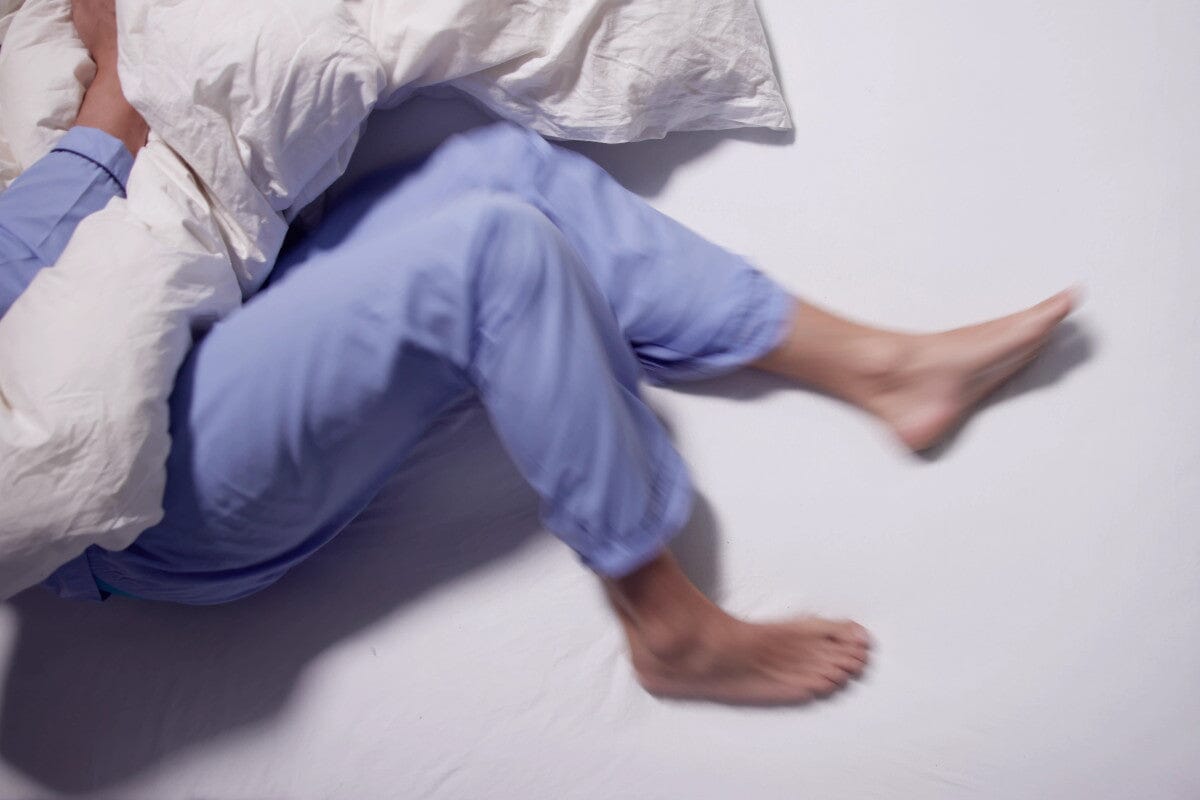 someone wearing blue pajamas, laying in bed as their legs move from RLS.