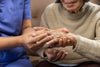 close-up of a nurse looking at an elderly woman's hand that has arthritis.