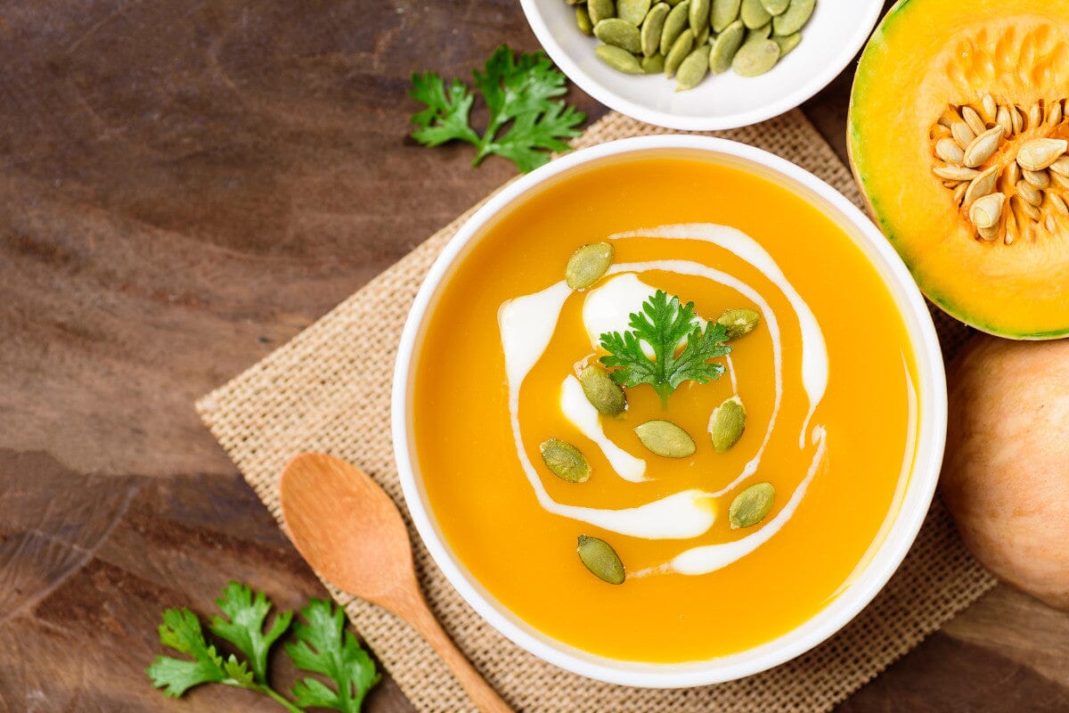 butternut squash soup in a white bowl sitting on a wooden table.