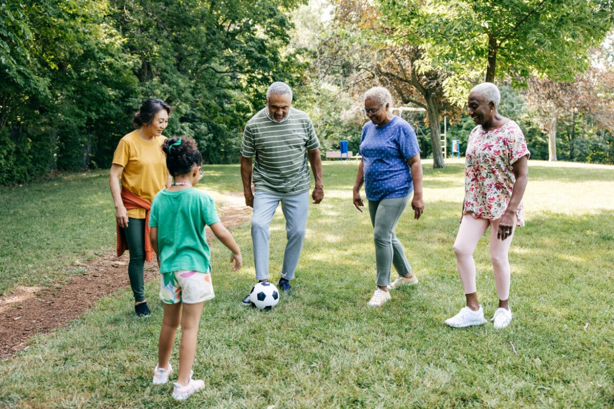 group of seniors playing soccer with a young kid