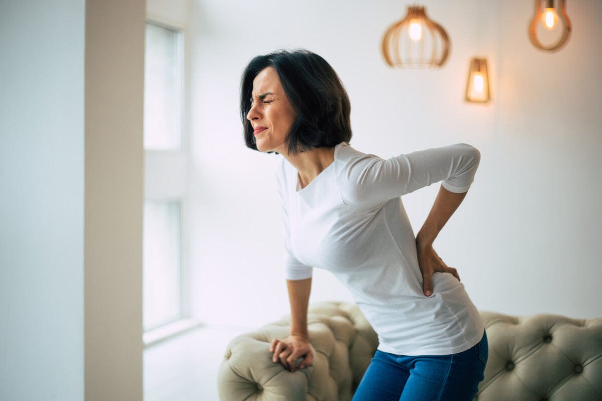 middle-aged woman gripping her lower back in pain.