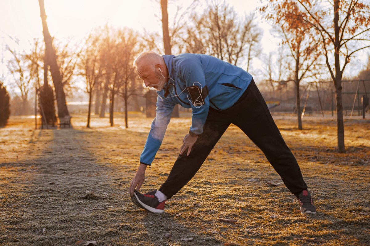 older man wearing athletic clothing, stretching outside in the crisp autumn air.