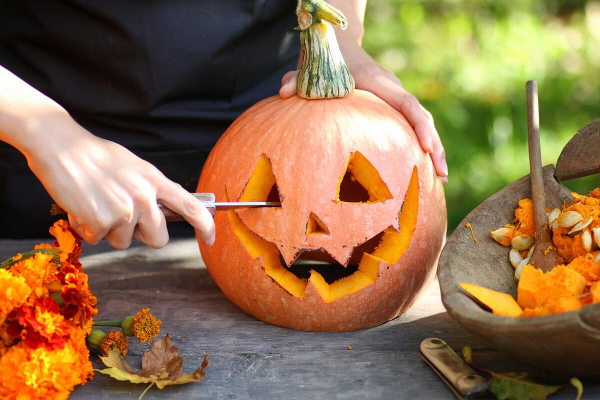 Hand carving a face into a pumpkin.