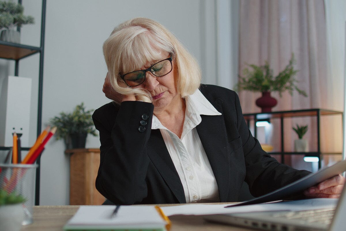 Tired sleepy senior business woman falling asleep sit at home office desk with computer