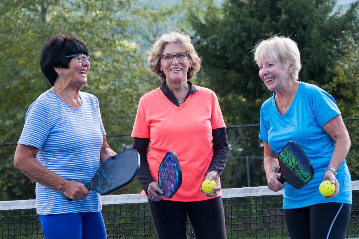 three senior ladies smiling and having a good time playing pickleball.