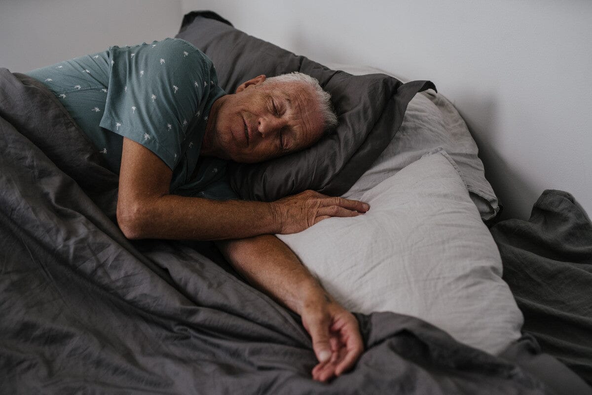 senior man sleeping peacefully under a gray comforter.