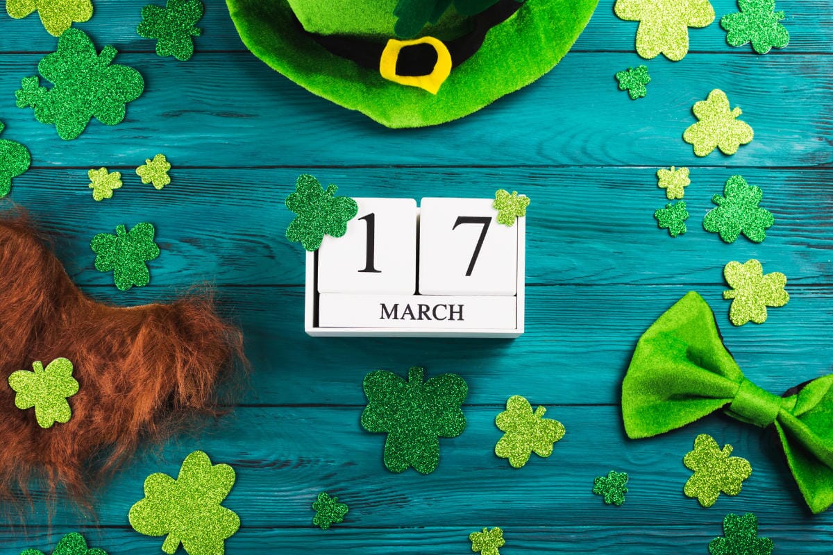 blue wooden background. shamrocks, an orange beard, a leprechaun hat, and a green bow tie surrounding