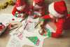 three kids wearing Christmas pajamas and Christmas hats laying on floor and coloring Christmas pages