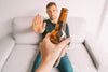 man sitting on couch, being offered a beer, but holding out his hand to say 