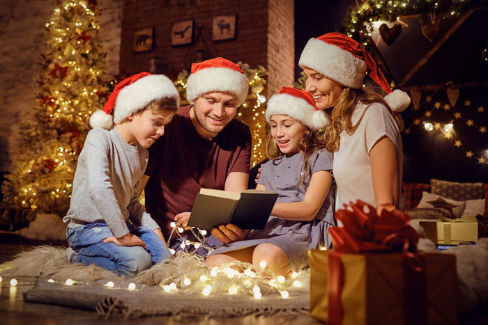 family wearing santa hats, sitting by the tree and reading a book