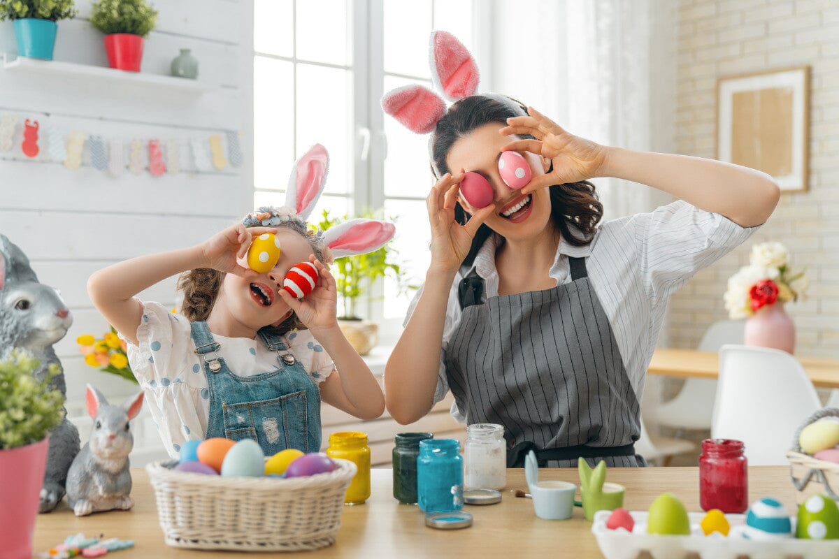 mother and daughter holding up Easter eggs over their eyes, wearing bunny ears