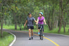 woman riding a bike next to a man running on the road surrounded by trees