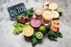 glasses of various juices sitting on table with fruits and veggies surrounding them