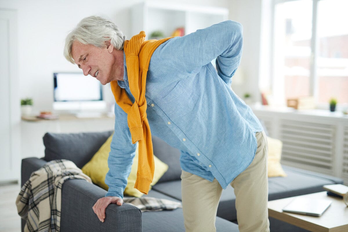 older man hunched over his couch, holding his back in pain