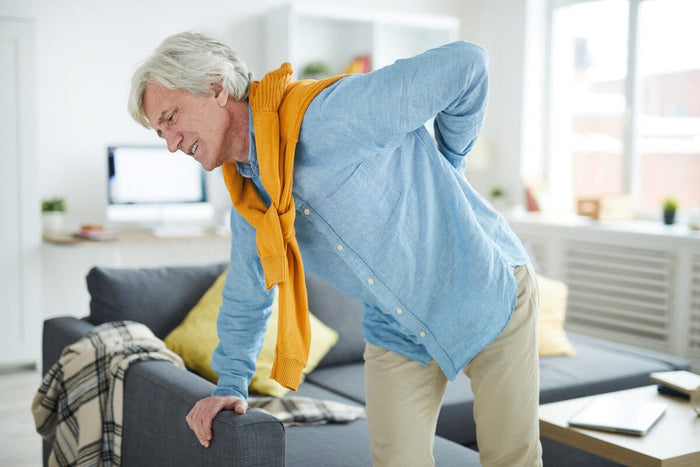 older man hunched over his couch, holding his back in pain