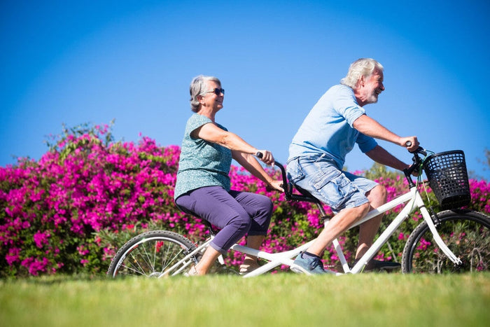 Happy senior couple riding a tandem-bicycle through pink spring flowers.