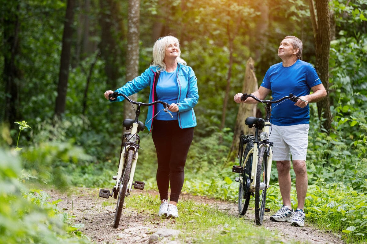 two seniors enjoying a ride on their bikes through the woods.