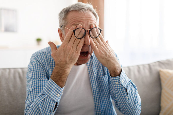 Senior man with glasses rubbing his eyes.