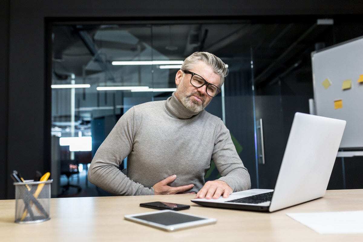 older man sitting at his desk, holding his stomach in pain