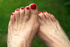 women's feet with bunions. red nail polish on her toes. green grass background.