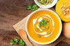 butternut squash soup in a white bowl sitting on a wooden table.