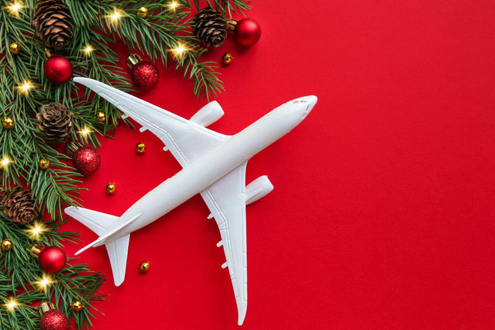 bright red background with pine tree needles, pine cones, red ornaments, twinkling lights, and a stark white small airplane