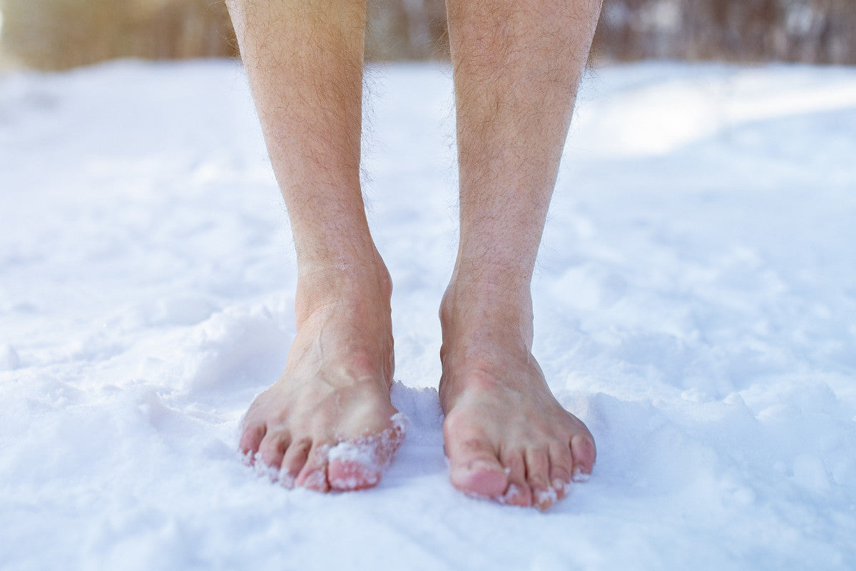 Senior guy standing barefoot on snow at winter forest