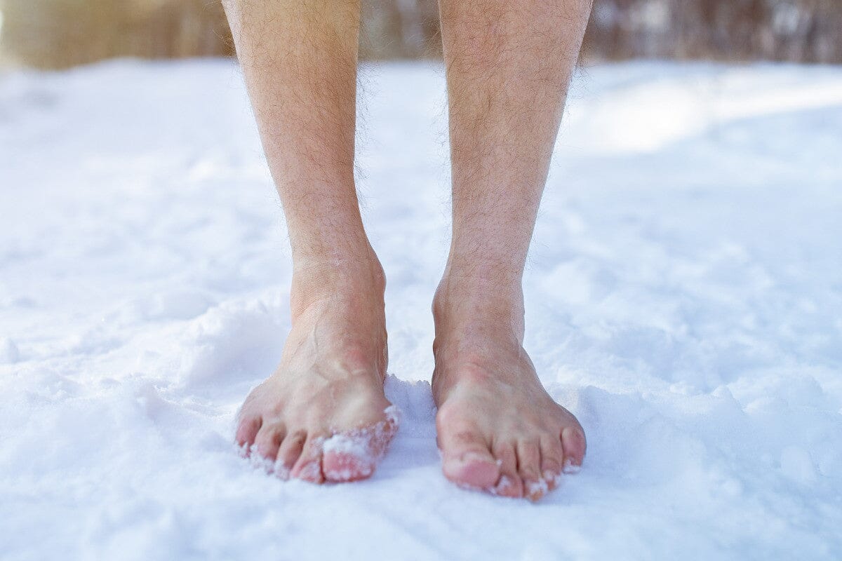 Senior guy standing barefoot on snow at winter forest