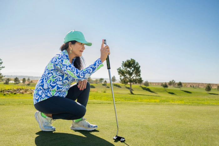 senior woman kneeling on the green with a golf club in her hand
