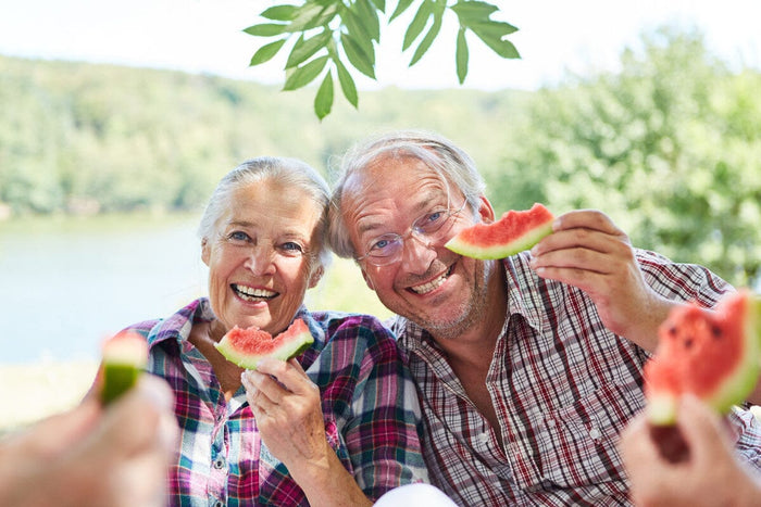 senior couple smiling and eating watermelon on the lake.