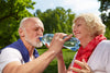 senior male drinking out of a water bottle outside.