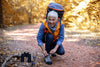 senior woman kneeling down and tying her shoe while on a hike in the fall.