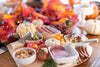 a charcuterie board with fall leaves, lights, and small pumpkins in the background