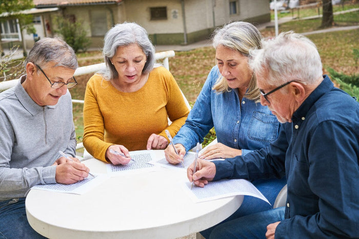 group of 4 seniors sitting a table outside, working on their own crossword puzzles and mazes.