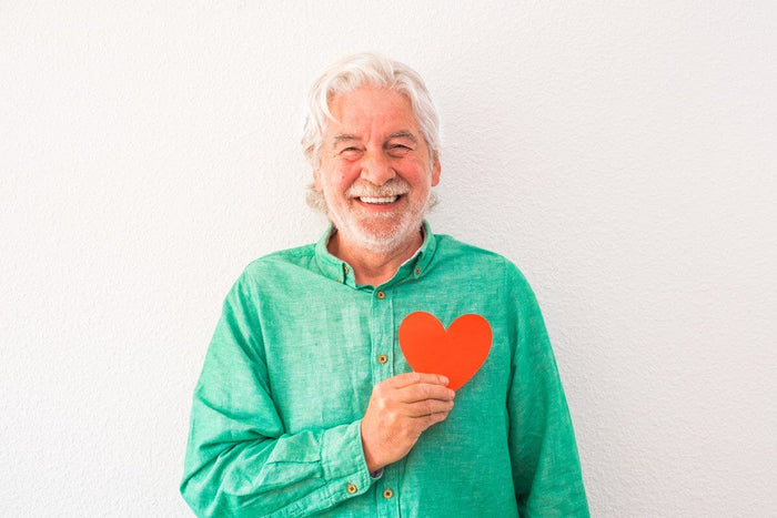 senior man smiling and holding a red paper heart.