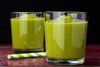 two short glasses filled with an avocado smoothie against a black background.