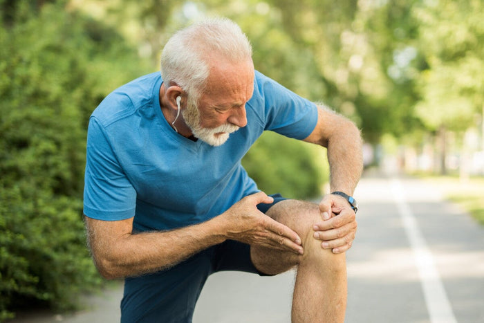 Senior man stopped to massage his knee while walking outside.