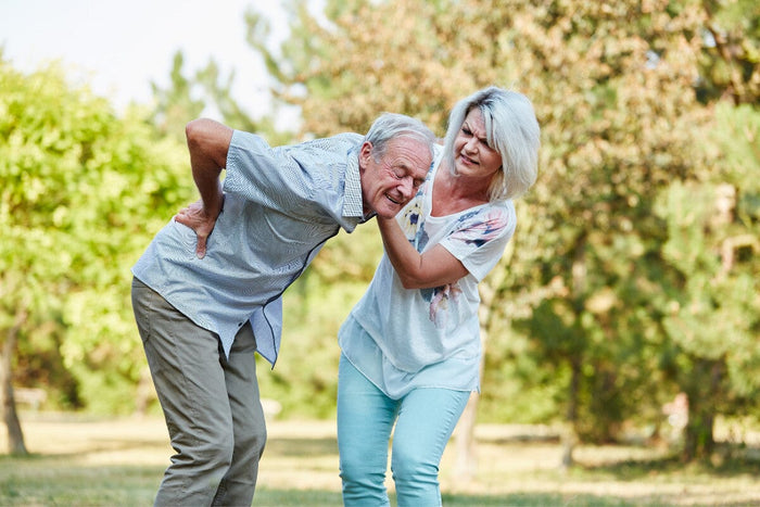 senior man bent over in pain from his hip. standing outside with his concerned wife.