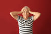 red background. Senior woman looking extremely stressed with her hands on her head.