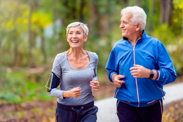 Senior couple jogging on a trail in a forest during late summer/early autumn. Wearing light jogging suits.