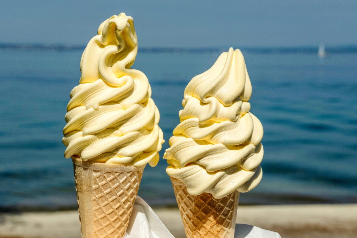 Light yellow, swirled ice cream in a waffle cone against a blue ocean background.