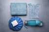 blue-gray damp towel, two different ice packs, water bottle on gray background.