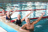 group of 4 seniors smiling and holding their left arms out while using their right arm to balance themselves on the edge of the pool that they're in