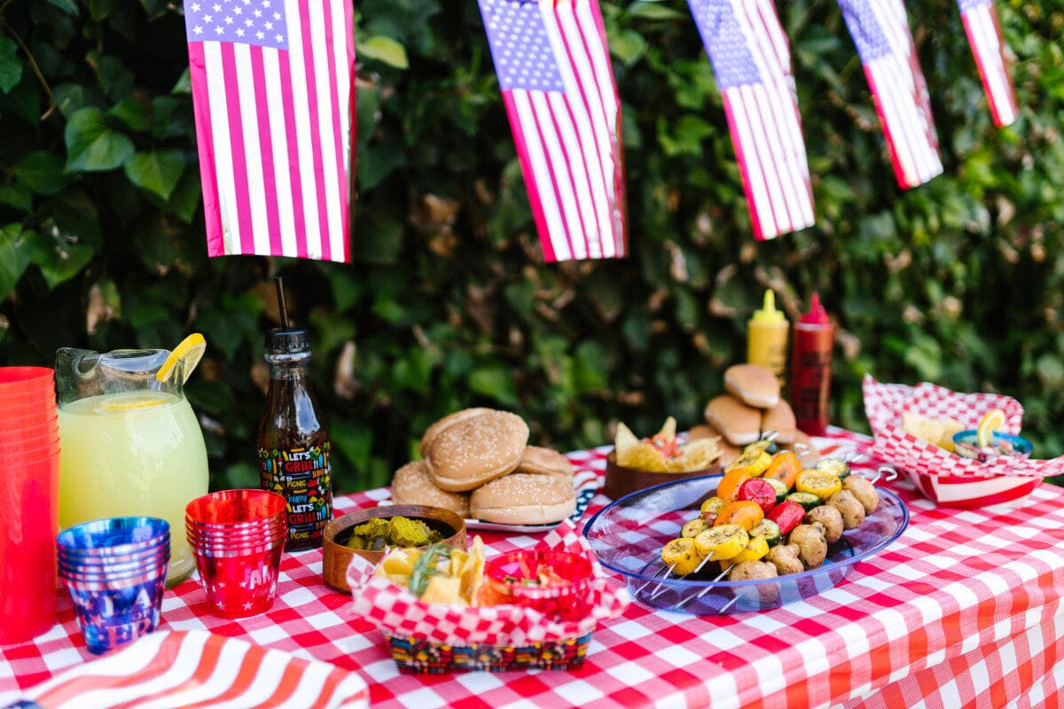 Table outside with various BBQ foods and American flags hanging above it.