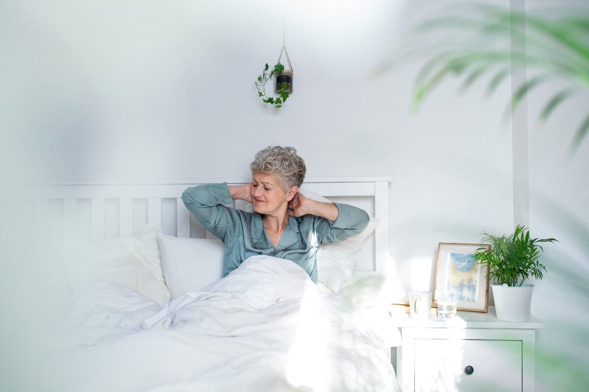senior woman with neck stiffness sitting in bed doing neck exercises.