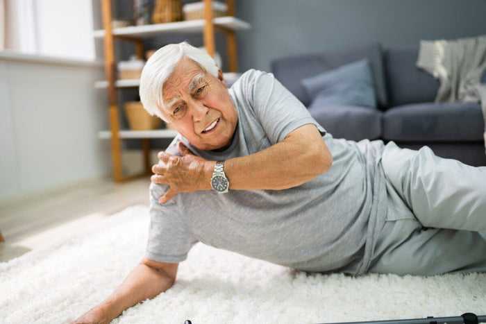 older man who fell and can't get up in the living room, touching his shoulder because he's in pain