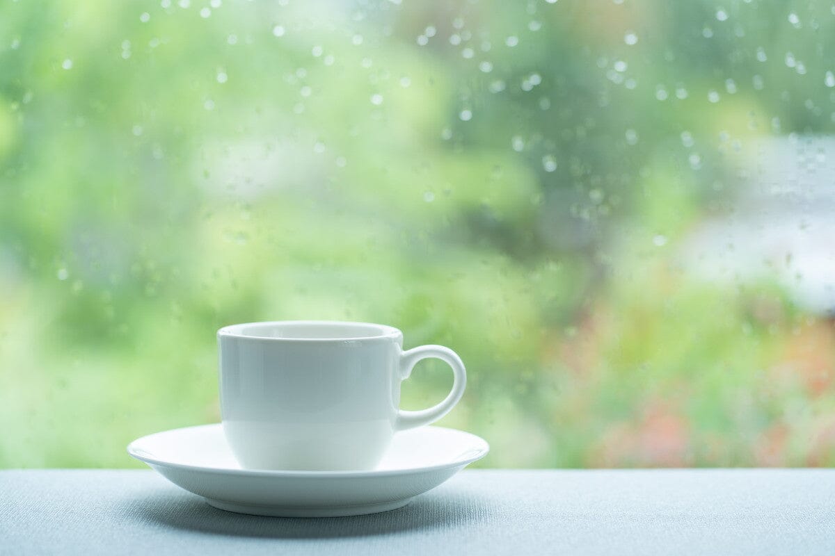 White coffee cup on white saucer on white window sill, rainy day.