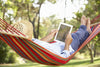 senior relaxing in a hammock reading a book.