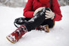 person sitting in the snow, wearing red boots, black pants, and a red coat, holding their knee in pain.