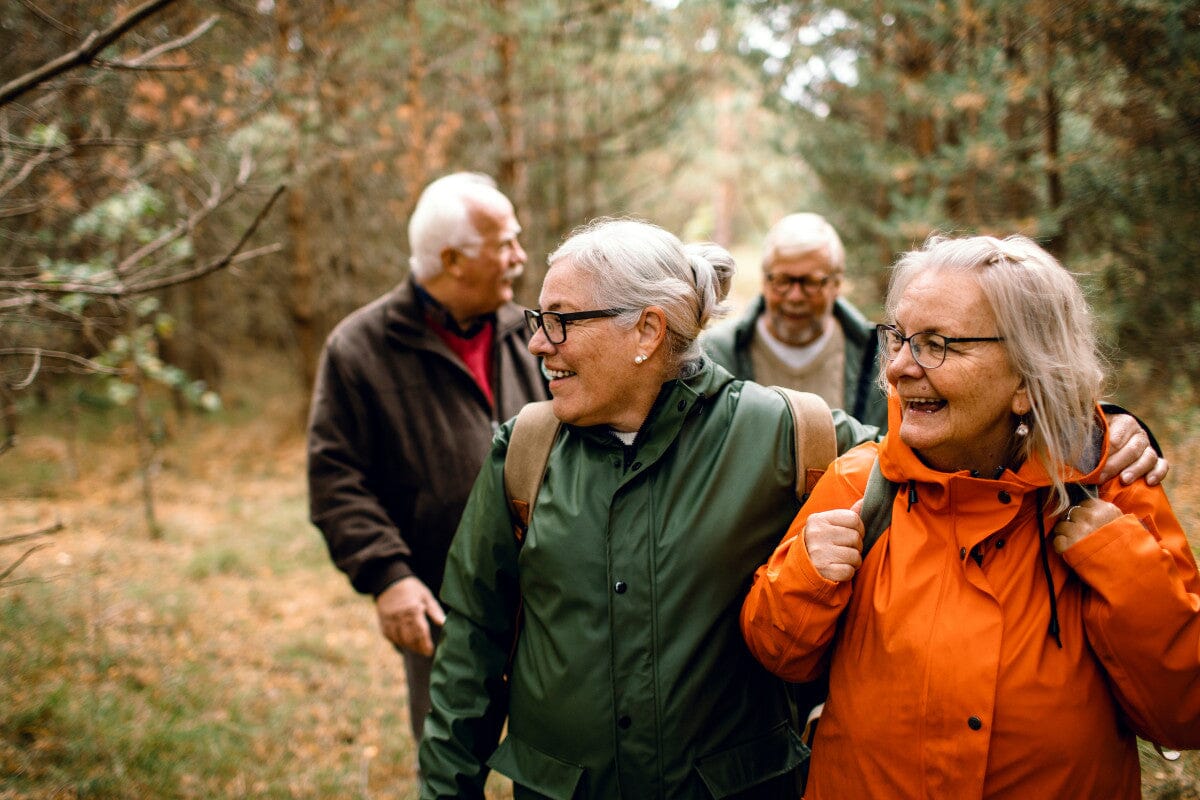 group of 4 seniors wearing light jackets as they hike through the forest during fall